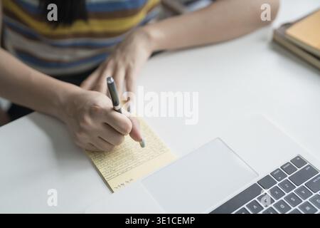 Online Tutoring Asian Girl in Headphones Engaged in Online Class with Laptop education writing homework study e-learning preparing for exam Stock Photo