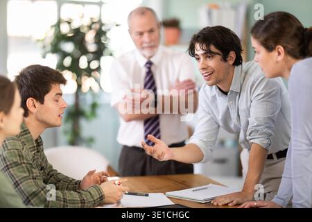 Students solving problems at table with teacher in background Stock Photo