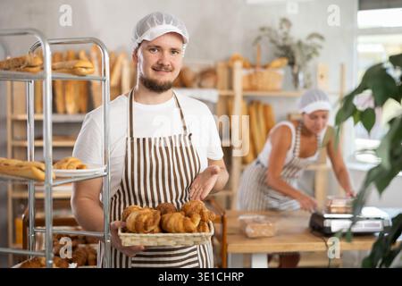Young salesman displays croissants in square wicker basket Stock Photo