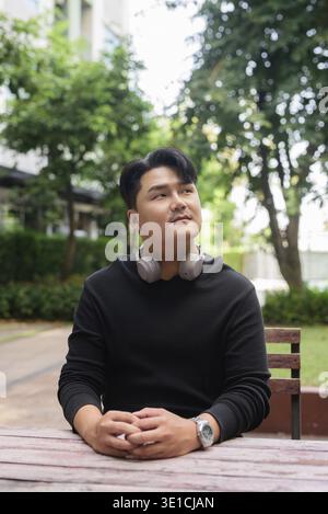 Portrait of Handsome Young Asian Man Sitting Outdoors in Park Concept Stock Photo