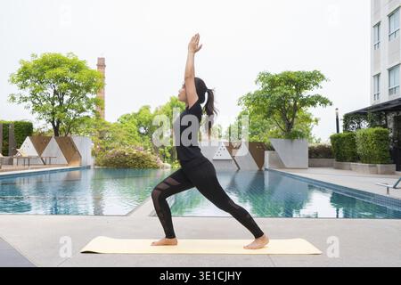 Young woman doing yoga outdoors next to swimming pool during summer Stock Photo