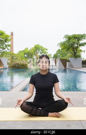 Young woman doing yoga outdoors next to swimming pool during summer Stock Photo