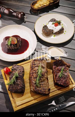A beautifully arranged display of gourmet steak dishes is set on a wooden table. Juicy steaks on a wooden platter, accompanied by sauce, vegetables, a Stock Photo