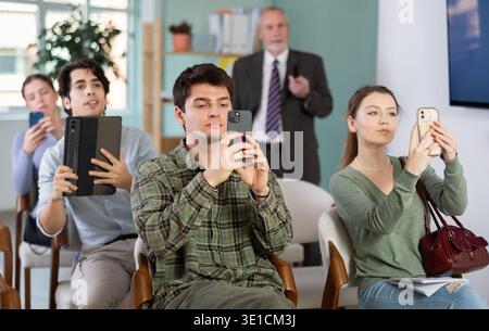 Students scanning QR code or taking photo, professor in background Stock Photo