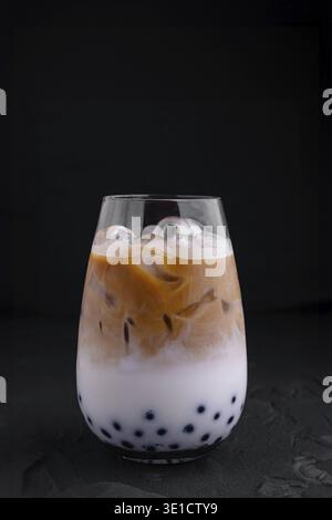 Iced coffee latte with milk and boba tapioca pearls is standing on black background Stock Photo