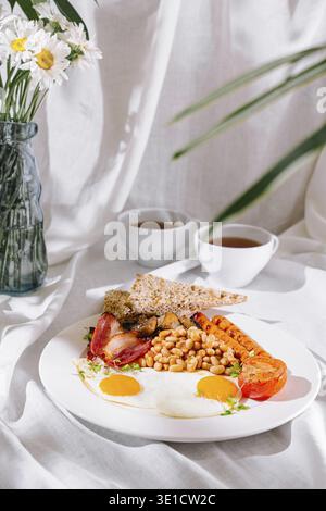Full english breakfast with fried eggs, sausages, beans, and toasts is served on white tablecloth Stock Photo