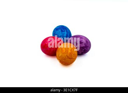 Four vibrantly colored Easter eggs in red, blue, purple, and orange arranged on a clean white background. The eggs display marbled dye patterns Stock Photo