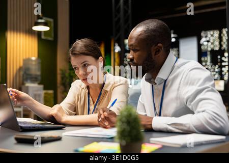 Team of businesspeople at office desk using laptop, evaluating operational metrics. Teamworking colleagues working late at night on notebook to assist online clients, finishing tasks Stock Photo