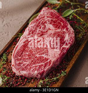 Raw, marbled ribeye steak adorned with herbs and spices, ready for cooking Stock Photo