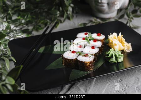 Sushi rolls set served on black plate decorated with greenery and chopsticks Stock Photo