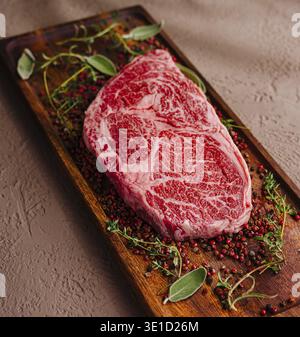 Raw, marbled ribeye steak adorned with herbs and spices, ready for cooking Stock Photo