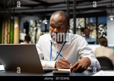 Checking reports, laptop and accountant in office writing down financial figures on paper. crosschecking data, notebook and focused businessman transcribing information from screen to notepad Stock Photo
