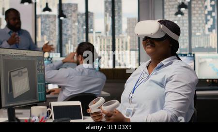 Engineer using virtual reality simulation to develop innovative solar powered device prototype. RD office professional uses VR headset to examining portable solar panel gadget, camera B Stock Photo