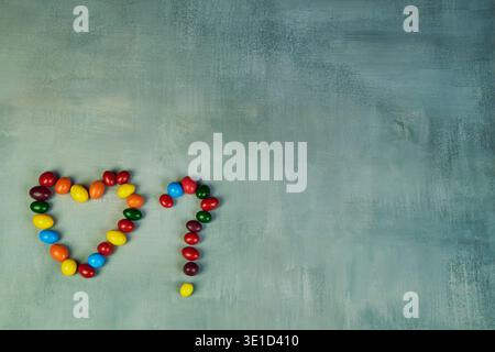 Colorful candies forming a heart shape and a question mark on textured background Stock Photo