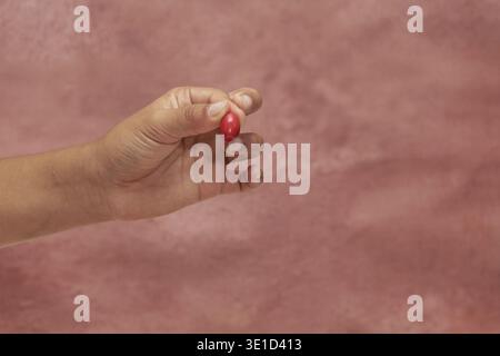 Child hand holding ripe red coffee cherry against pink background Stock Photo