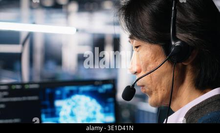 Engineer in data center wearing headset assisting users with AI enhanced troubleshooting. Server room employee managing support tickets using automated response systems, camera A Stock Photo