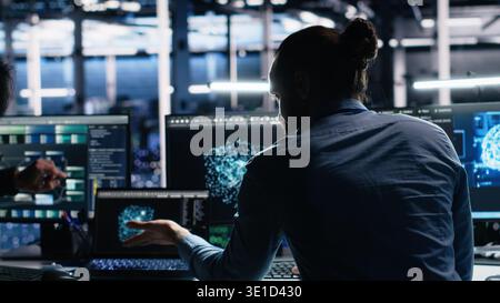 Data center system administrators use PC to monitor neural network using AI LLM. Asian man and colleague at work using artificial intelligence to oversee servers powering machine learning, camera A Stock Photo
