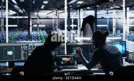 Senior programmer and coworker in data center coding with generative AI assistance. Teamworking colleagues leveraging artificial intelligence large language model to solve tasks, camera A Stock Photo