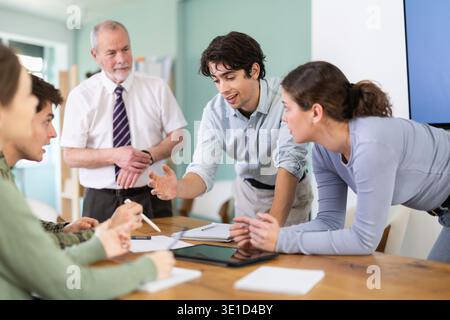 Students solving problems at table with teacher in background Stock Photo