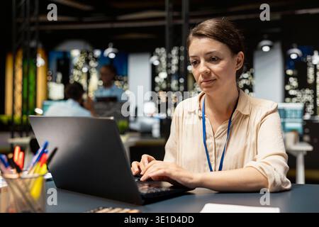 Female employee in office completing spreadsheets on laptop, inputting and analyzing data. Woman typing on notebook keyboard, browsing internet, researching information online, working overnight Stock Photo