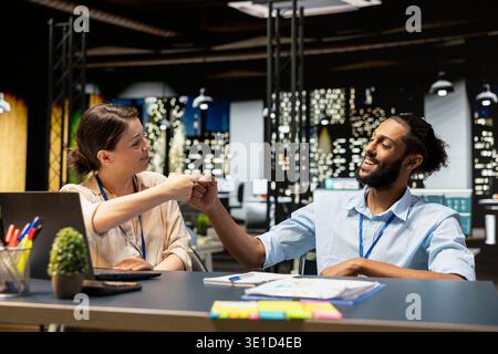 Cheerful office coworkers doing fist bump, pleased by business results after analyzing data on laptop. Jolly Arab man and colleague celebrate positive financial figures in workplace on notebook Stock Photo