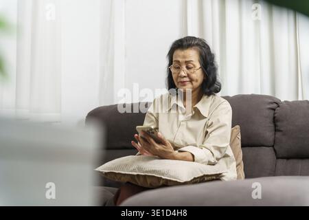 Middle age Asian woman holding cell telephone. senior woman with smart phone. elderly woman using smartphone at home with technology concept Stock Photo
