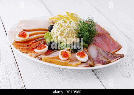 Sliced fish platter with butter, lemon and olives is served on a white wooden table Stock Photo