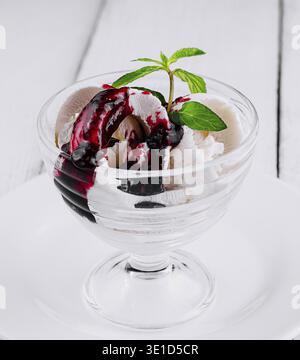 Glass dish with vanilla ice cream and berry sauce is topped with a sprig of mint Stock Photo