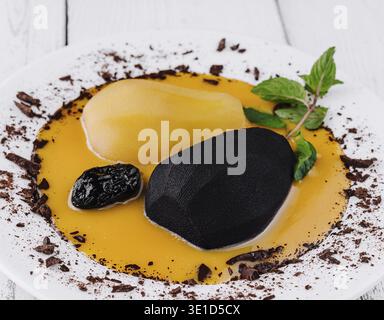 Pears poached in black and white served on a white plate with orange sauce and decorated with chocolate and mint leaves Stock Photo