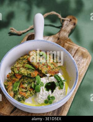 Freshly made veggie patties served with a creamy yogurt sauce in a ceramic bowl on a wooden board Stock Photo