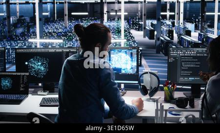 Teamworking engineers doing brainstorming in data center, reviewing AI diagnostics on computer. Team of IT expert working together in server room, optimizing artificial intelligence systems, camera A Stock Photo