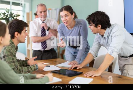 Students solving problems at table with teacher in background Stock Photo