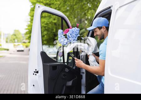 Happy courier inside the white van during flowers delivery is waiting for a client Stock Photo
