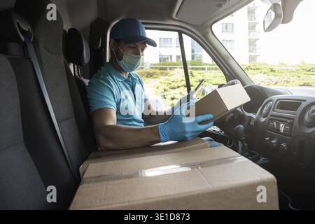 Young courier man in a van is checking packages and waybill using tablet pc before delivery Stock Photo
