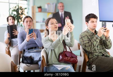 Students scanning QR code or taking photo, professor in background Stock Photo