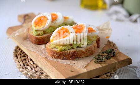 Two slices of crusty sourdough bread topped with smashed avocado and vibrant soft boiled eggs. Soft natural morning light highlights the creamy textur Stock Photo