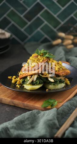 Two slices of golden-brown tofu are served over wilted greens and onions with a textured breadcrumb garnish. The scene features soft side lighting, ru Stock Photo