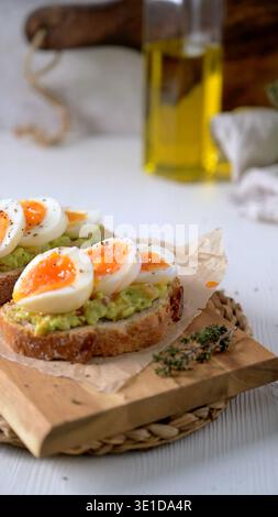 A close up shot of vibrant avocado mash on crusty sourdough bread topped with jammy soft boiled eggs and black pepper. Bright natural lighting highlig Stock Photo