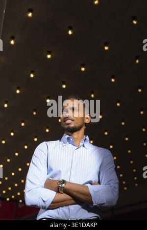 Low angle view shot of handsome black African businessman outdoors in city during summer smiling and thinking vertical shot Stock Photo