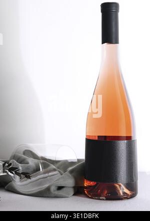 Elegant bottle of rose wine with blank black label for mockup and empty wineglass laying on tablecloth Stock Photo