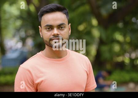 Portrait of young handsome bearded Indian man at the park outdoors Stock Photo