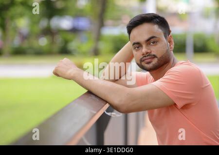 Portrait of young handsome bearded Indian man at the park outdoors Stock Photo