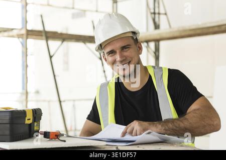 Young is worker checking blueprints during his work on a construction site Stock Photo