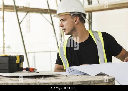 Young is worker checking blueprints during his work on a construction site Stock Photo