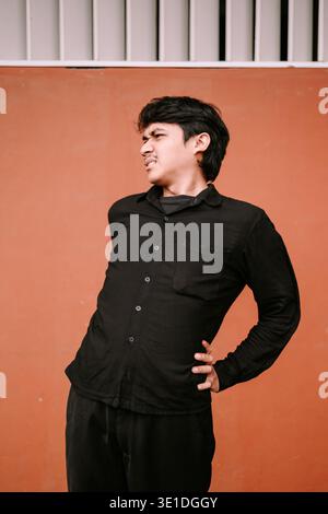 Young man experiencing severe lower back pain, clutching his side with a grimacing expression. He stands against a simple, warm-toned wall, highlighti Stock Photo