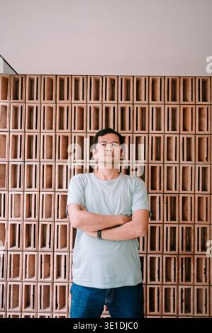 A man with dark hair and a light t-shirt stands confidently with crossed arms, looking directly at the camera. He is set against a modern, textured te Stock Photo