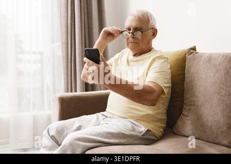 Senior man wearing eyeglasses is using smartphone at home Stock Photo