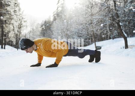 Athletic man doing push ups during his calisthenics winter workout in snowy park Stock Photo