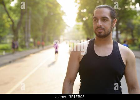 Portrait of young handsome bearded Indian man relaxing at the park Stock Photo