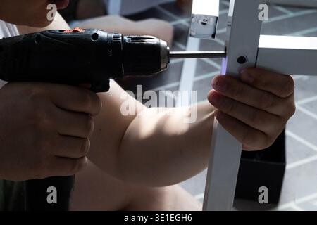 Man using power drill to assemble furniture frame at home, DIY furniture installation Stock Photo